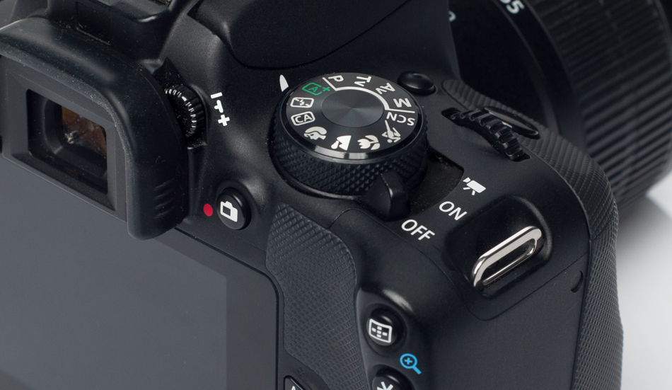 Canon 100D. W lewym górnym rogu zdjęcia znajduje się guzik do regulacji wizjera.
